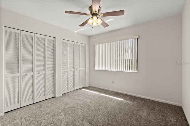 unfurnished bedroom featuring carpet flooring, ceiling fan, two closets, and baseboards