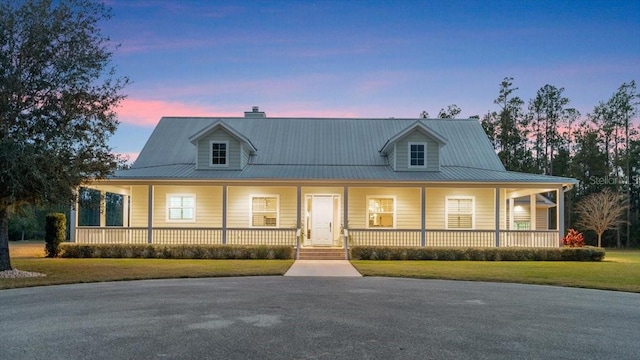 country-style home featuring covered porch, metal roof, and a yard