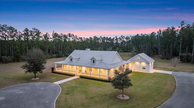 view of front of home with a porch, a front yard, driveway, and a wooded view