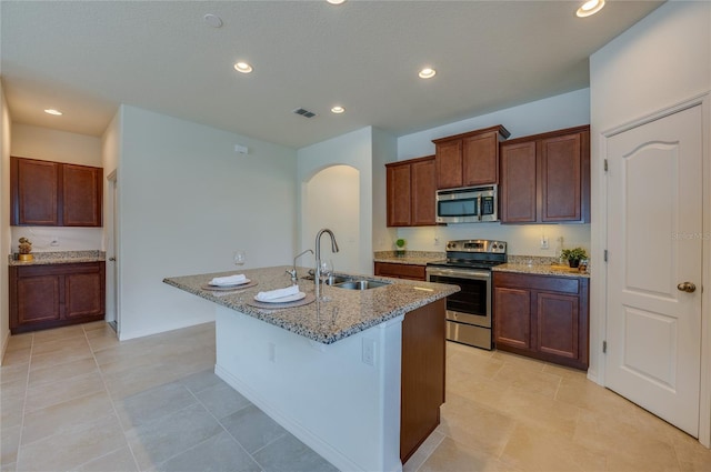 kitchen with stainless steel appliances, sink, a center island with sink, and light stone counters