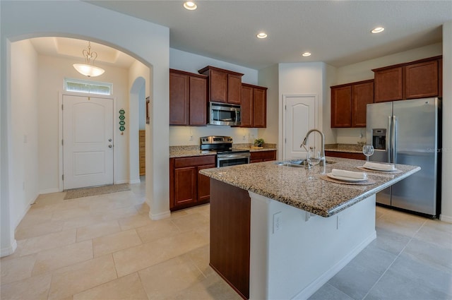 kitchen with a kitchen bar, sink, light stone counters, stainless steel appliances, and a kitchen island with sink