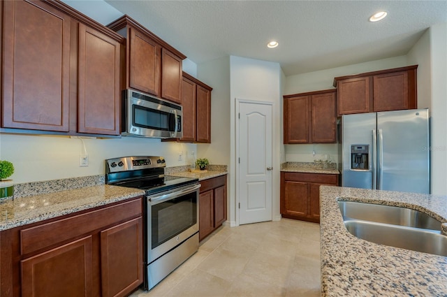 kitchen featuring light stone countertops, appliances with stainless steel finishes, sink, and a textured ceiling