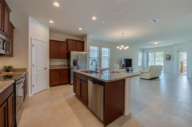 kitchen featuring pendant lighting, sink, stainless steel appliances, light stone countertops, and a center island with sink