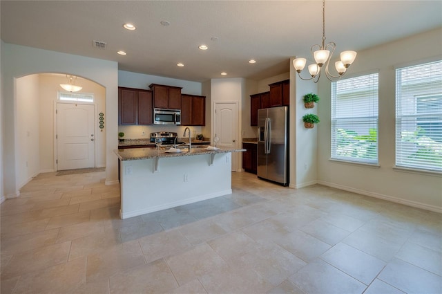 kitchen with appliances with stainless steel finishes, a breakfast bar, pendant lighting, dark stone counters, and a center island with sink