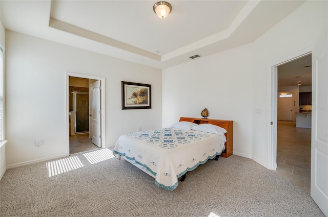 carpeted bedroom with a raised ceiling and ensuite bath