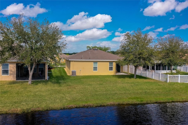 rear view of property with cooling unit, a lawn, and a water view