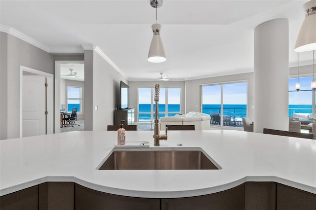 kitchen featuring light stone counters, a sink, open floor plan, hanging light fixtures, and crown molding