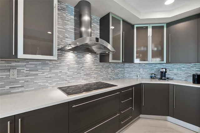 kitchen featuring wall chimney exhaust hood, marble finish floor, black electric cooktop, light countertops, and backsplash