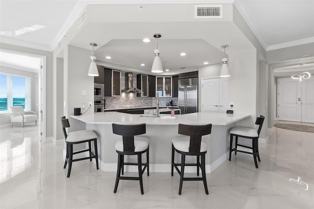 kitchen featuring visible vents, wall chimney exhaust hood, built in appliances, crown molding, and a sink