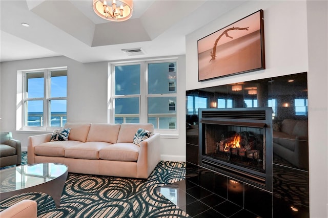 living room with a raised ceiling, visible vents, an inviting chandelier, a lit fireplace, and baseboards