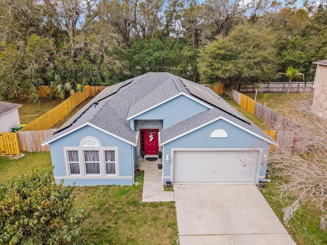 view of front facade featuring solar panels, a garage, a fenced backyard, driveway, and a front lawn