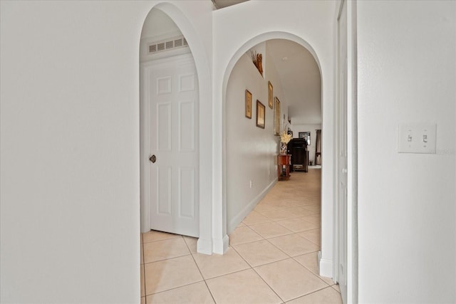 hallway featuring arched walkways, light tile patterned floors, visible vents, and baseboards