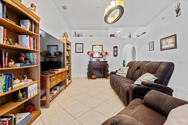 living area with light tile patterned floors, arched walkways, visible vents, vaulted ceiling, and a glass covered fireplace