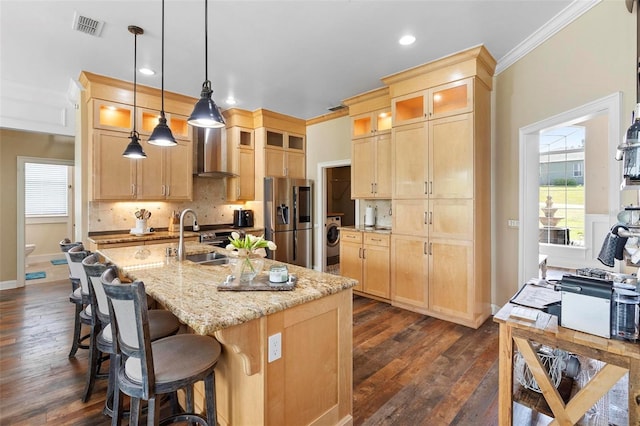 kitchen featuring a center island with sink, stainless steel fridge with ice dispenser, sink, washer / dryer, and wall chimney exhaust hood