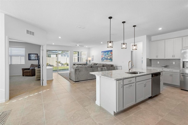 kitchen featuring a kitchen island with sink, stainless steel appliances, light stone countertops, sink, and backsplash