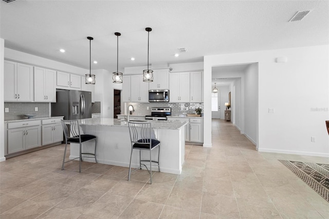 kitchen featuring a center island with sink, stainless steel appliances, light stone countertops, decorative light fixtures, and sink