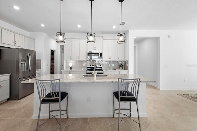 kitchen with sink, light stone counters, stainless steel appliances, hanging light fixtures, and an island with sink