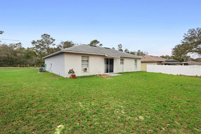 rear view of property with stucco siding, a lawn, central AC unit, fence, and cooling unit