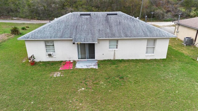 rear view of house featuring cooling unit, roof with shingles, a lawn, and stucco siding