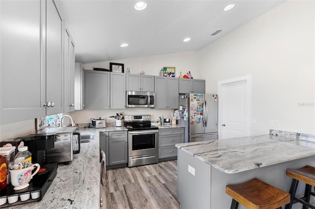 kitchen with appliances with stainless steel finishes, light stone countertops, a breakfast bar area, and kitchen peninsula