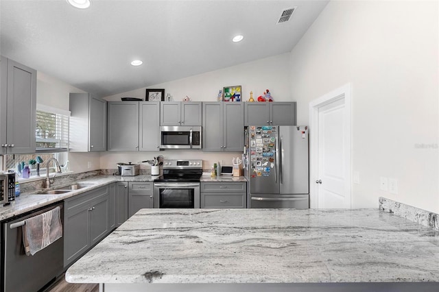 kitchen featuring appliances with stainless steel finishes, sink, vaulted ceiling, and light stone countertops