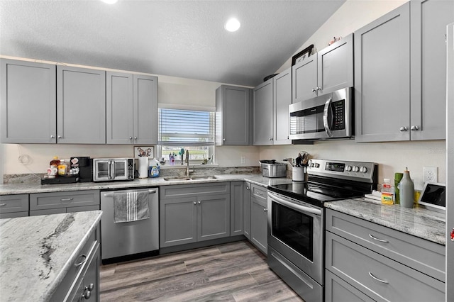 kitchen with sink, appliances with stainless steel finishes, gray cabinetry, and light stone countertops