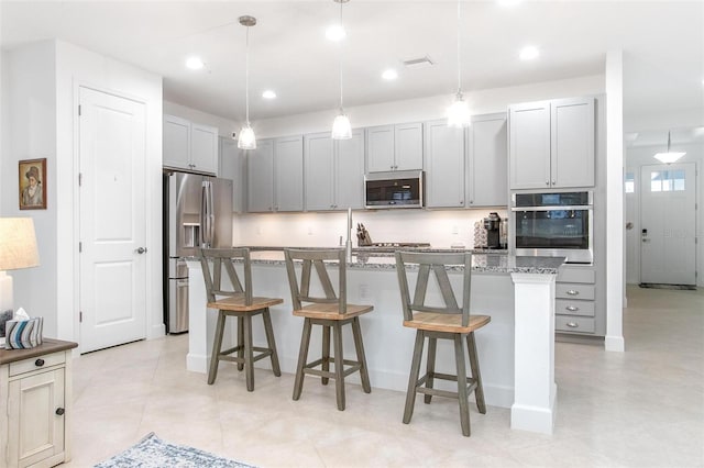 kitchen featuring stainless steel appliances, an island with sink, decorative light fixtures, and a kitchen breakfast bar