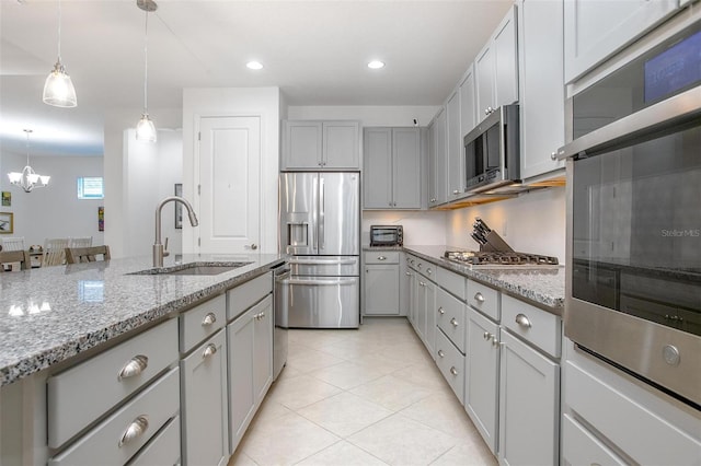 kitchen with appliances with stainless steel finishes, light stone countertops, gray cabinets, pendant lighting, and a sink