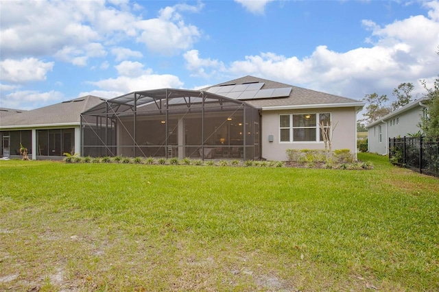 rear view of house with roof mounted solar panels, a lawn, fence, and stucco siding