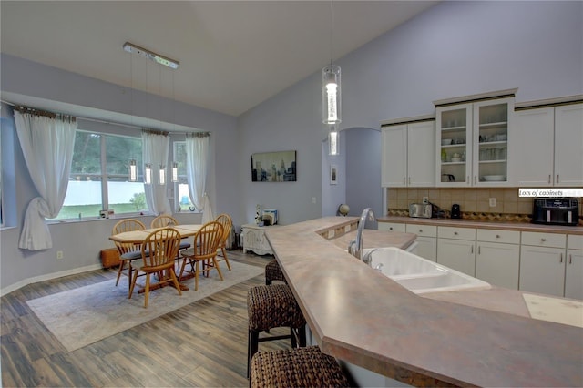 kitchen featuring a breakfast bar area, glass insert cabinets, hanging light fixtures, white cabinetry, and a sink