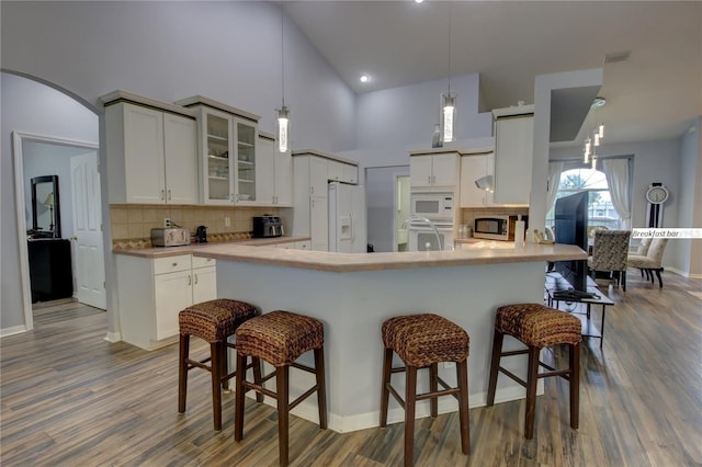 kitchen with arched walkways, light countertops, glass insert cabinets, white cabinetry, and white appliances