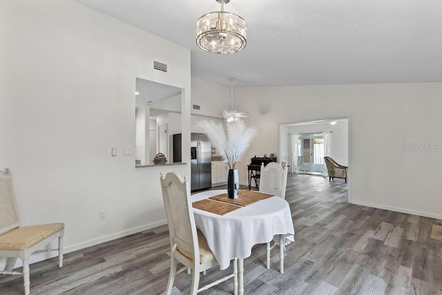 dining space featuring ceiling fan with notable chandelier, wood-type flooring, and lofted ceiling