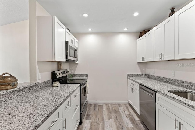 kitchen with white cabinetry, light stone countertops, stainless steel appliances, and light hardwood / wood-style floors