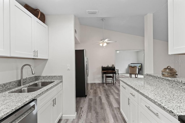 kitchen with stainless steel appliances, light stone counters, white cabinets, vaulted ceiling, and sink