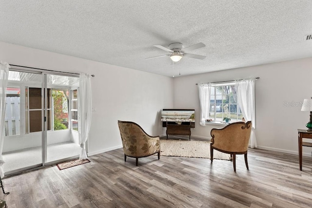 living area featuring ceiling fan, wood-type flooring, and a textured ceiling