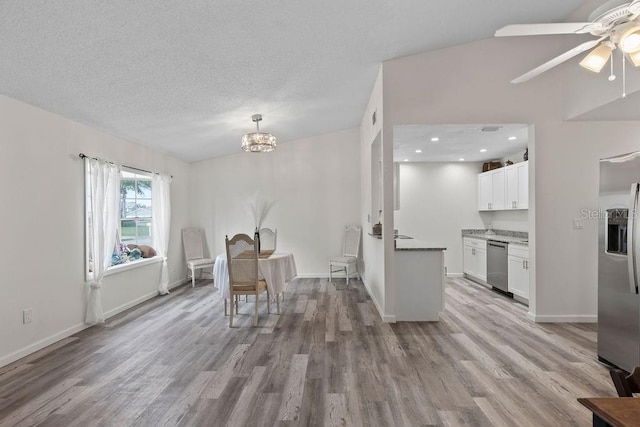 unfurnished dining area with ceiling fan with notable chandelier, light wood-type flooring, and a textured ceiling