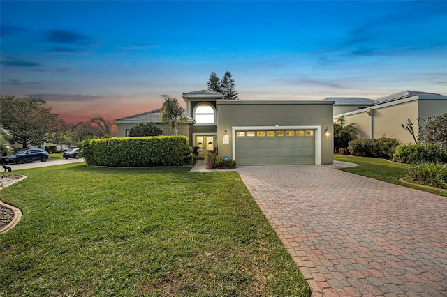 view of front of house featuring decorative driveway, a front yard, an attached garage, and stucco siding