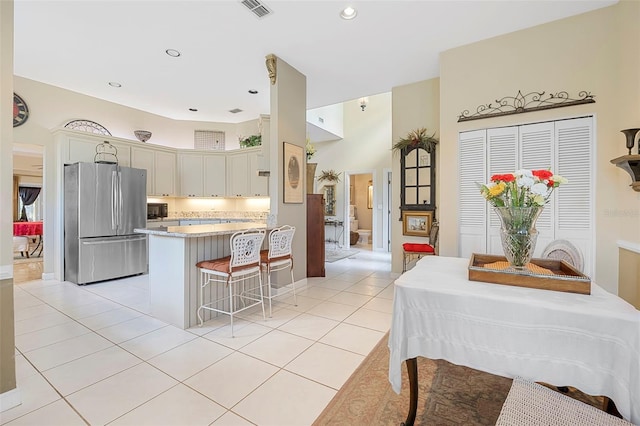 kitchen with cream cabinetry, light tile patterned floors, visible vents, freestanding refrigerator, and black microwave