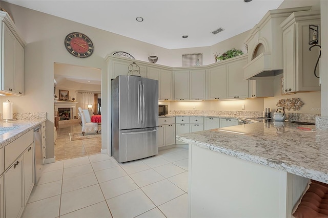 kitchen featuring light stone counters, a fireplace, visible vents, appliances with stainless steel finishes, and light tile patterned flooring