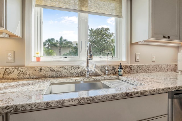 kitchen with light stone countertops, stainless steel dishwasher, and a sink