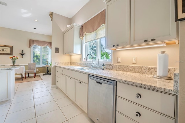 kitchen with stainless steel dishwasher, white cabinets, light tile patterned flooring, a sink, and light stone countertops