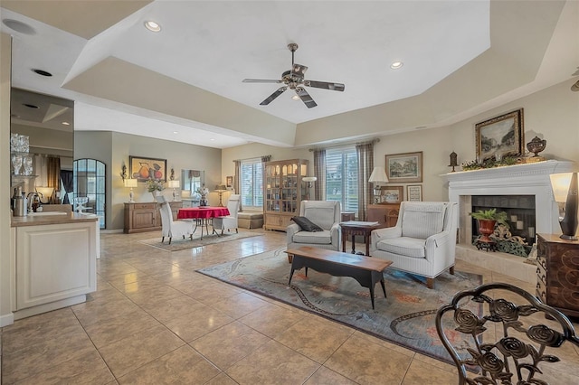 interior space with light tile patterned floors, a fireplace, a raised ceiling, and a ceiling fan