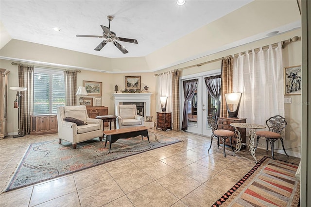 living area featuring light tile patterned floors, a tray ceiling, a tile fireplace, and a ceiling fan