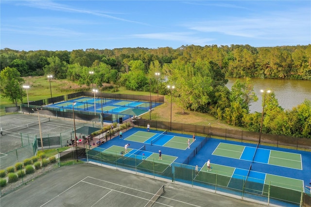 view of tennis court featuring a water view, a forest view, and fence