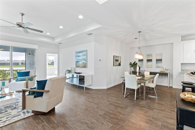 living room with dark hardwood / wood-style flooring, ceiling fan, and a raised ceiling