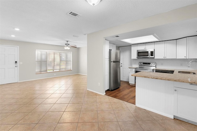 kitchen featuring light stone counters, stainless steel appliances, visible vents, white cabinetry, and a sink