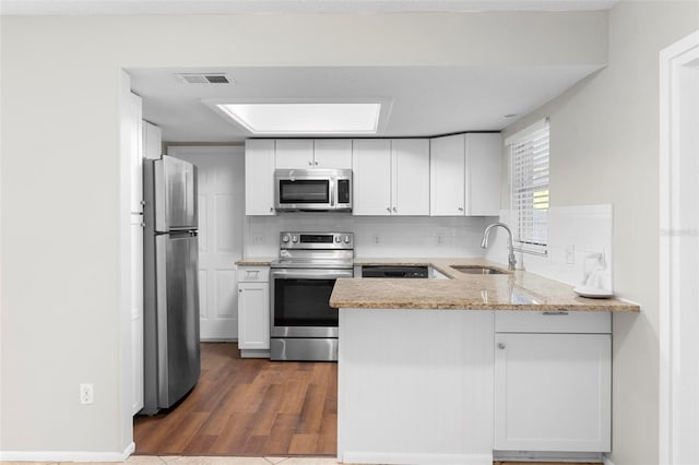 kitchen featuring tasteful backsplash, white cabinets, appliances with stainless steel finishes, light stone counters, and a sink