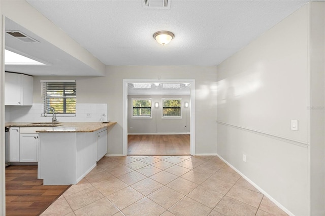 kitchen featuring a peninsula, a sink, visible vents, white cabinets, and decorative backsplash