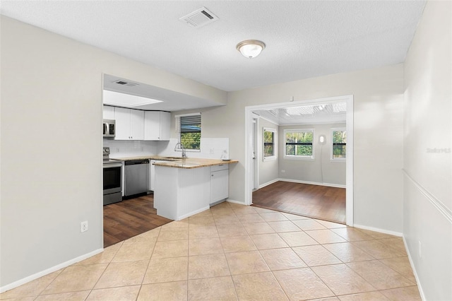 kitchen featuring visible vents, appliances with stainless steel finishes, a peninsula, light countertops, and white cabinetry