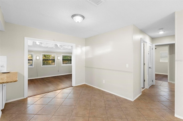 spare room featuring visible vents, light tile patterned flooring, a textured ceiling, and baseboards